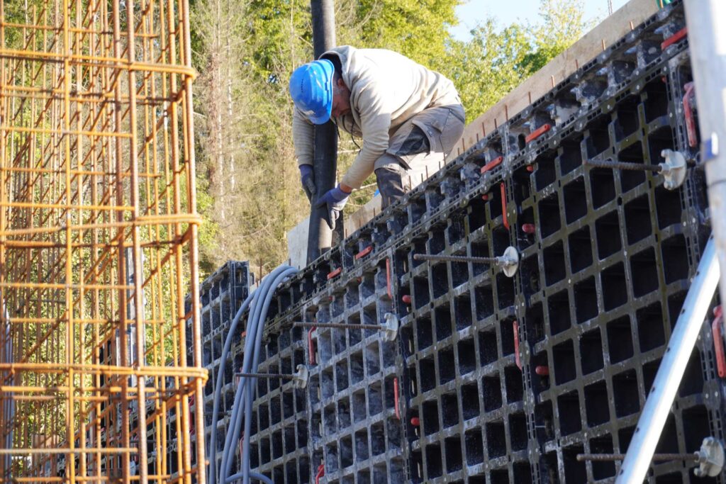 A construction worker wearing a blue hard hat is intently filling a formwork made of black mesh