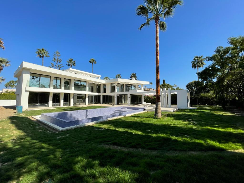 A modern white house with large glass windows and an empty pool in the sunny garden