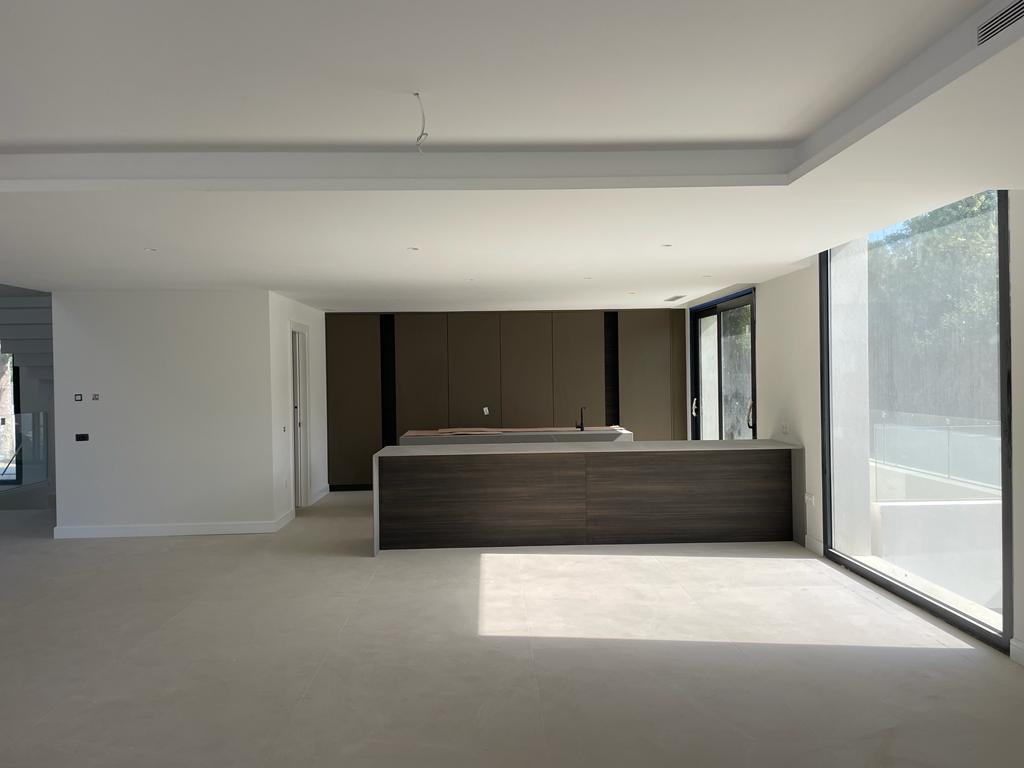 A bright, modern living room with large windows and an open kitchen in earth tones