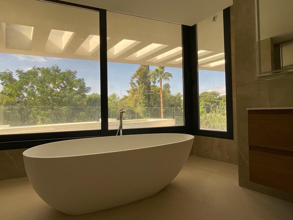 An elegant freestanding white bathtub in front of large windows overlooking the greenery